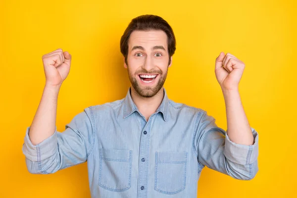 Retrato fotográfico de un joven sonriente haciendo gestos como ganador con camisa de mezclilla aislada sobre fondo de color amarillo brillante —  Fotos de Stock