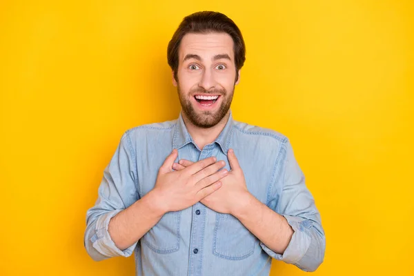 Foto portret van de jongeman glimlachend dolblij het houden van handen op de borst verbaasd geïsoleerd op felgele kleur achtergrond — Stockfoto