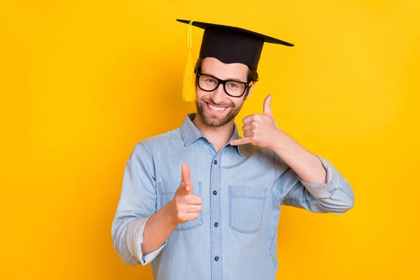 Foto av ung man glad leende visa fingrar kallar du tecken bära hatt master examen isolerad över gul färg bakgrund — Stockfoto