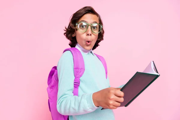 Fotografie šokovaný chlapec držet učebnici otevřené ústa nosit brýle taška košile izolované růžové barvy pozadí — Stock fotografie