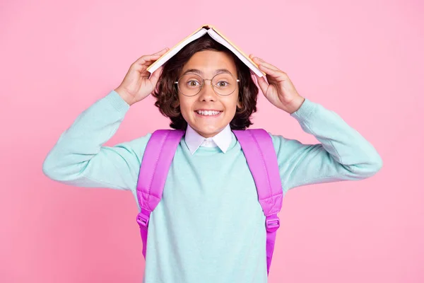 Photo of cheerful funny boy hold book cover head toothy smile wear bag teal shirt isolated pink color background — Stock Photo, Image