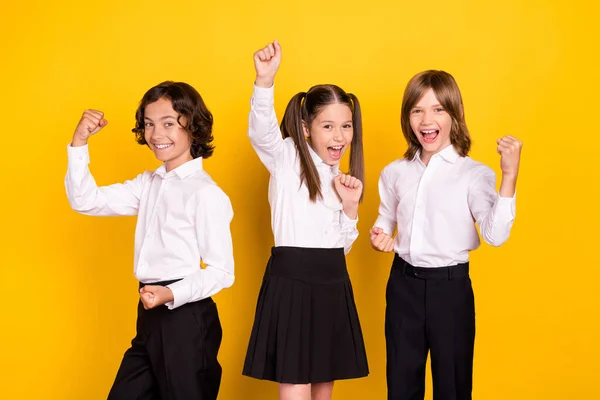 Foto van drie verbaasd schoolkinderen vieren overwinning dragen witte shirt geïsoleerde gele kleur achtergrond — Stockfoto