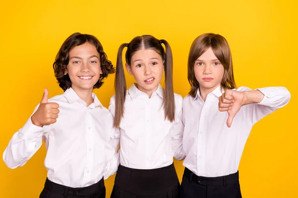 Foto de escolares dudosos inseguros formalwear levantamiento mostrando pulgar hacia arriba pulgar hacia abajo aislado color amarillo fondo —  Fotos de Stock