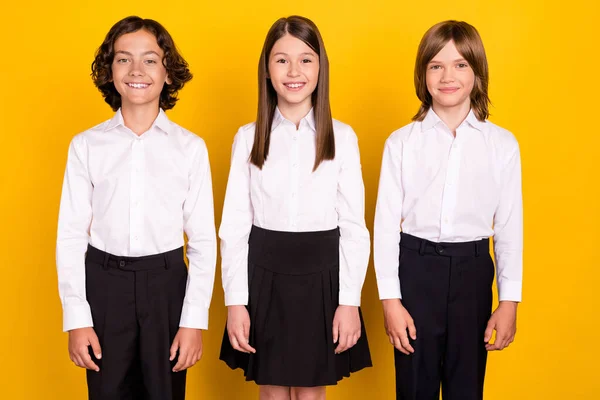 Foto de tres escolares toothy radiante sonrisa posando desgaste camisa blanca aislado color amarillo fondo — Foto de Stock