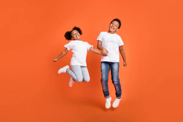 Foto in voller Größe von kleinen lustigen Mädchen Junge springen tragen weißes T-Shirt Jeans Turnschuhe isoliert auf orangefarbenem Hintergrund — Stockfoto