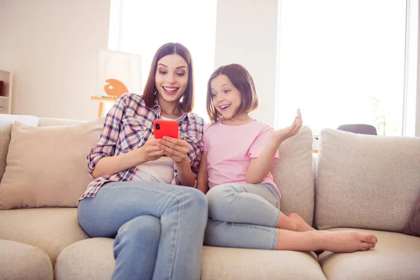 Retrato de dos chicas alegres atractivas sentadas en diván usando dispositivo gadget divertirse en casa plana en el interior —  Fotos de Stock