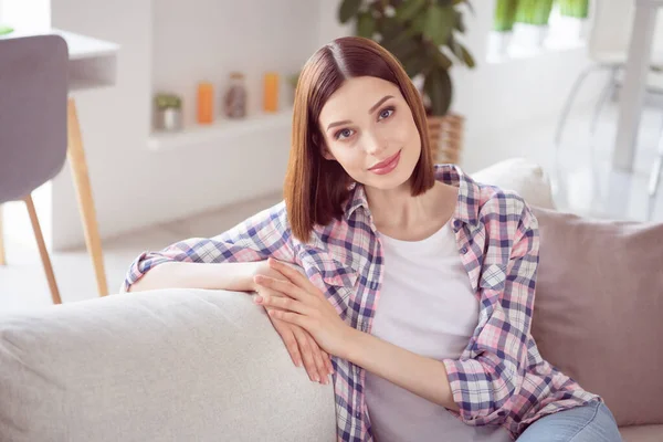 Портрет привлекательной спокойной мирной девушки, проводящей свободное время сидя на диване, отдыхая дома в помещении — стоковое фото