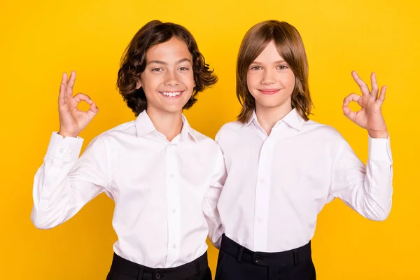 Foto de escolares encantadores divertidos usan uniforme sonriente mostrando signos okey aislado color amarillo fondo — Foto de Stock