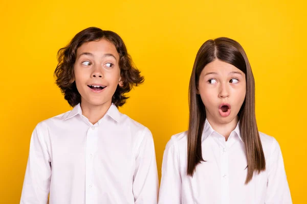 Фото впечатленных сладких школьников формальной одежды большие глаза глядя друг на друга с открытым ртом изолированный желтый цвет фона — стоковое фото