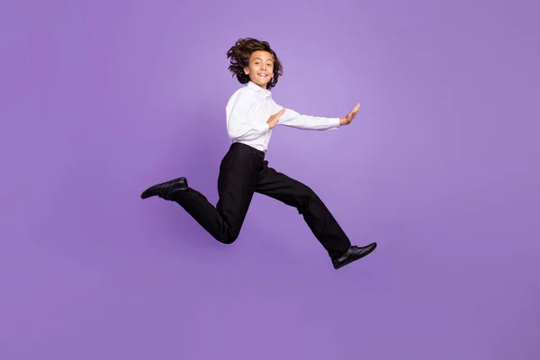 フルサイズの写真のクールな小さなブルネット少年ジャンプ戦い服シャツパンツスニーカー隔離された紫色の背景 — ストック写真