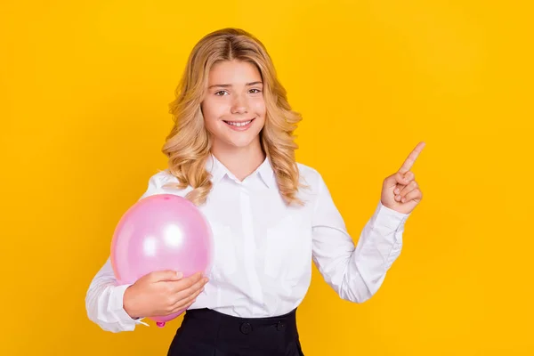 Foto van schoolmeisje directe vinger lege ruimte houden ballon dragen witte shirt geïsoleerde gele kleur achtergrond — Stockfoto