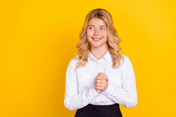 Фото допитливої мрійливої школярки, яка тримає руки, виглядають порожніми, одягнені в білі сорочки ізольовані жовтого кольору фону — стокове фото
