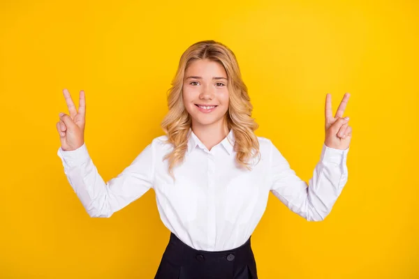 Foto van positieve schoolmeisje tonen twee v-tekens glans glimlach dragen witte shirt geïsoleerde gele kleur achtergrond — Stockfoto