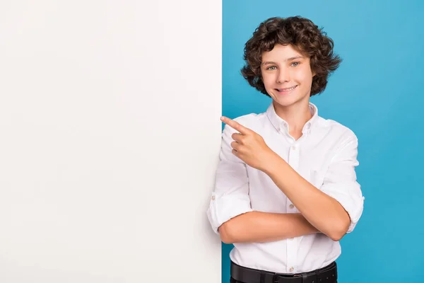 Foto de muito bonito menino da escola desgaste branco camisa apontando dedo cartaz vazio espaço sorrindo isolado azul cor fundo — Fotografia de Stock