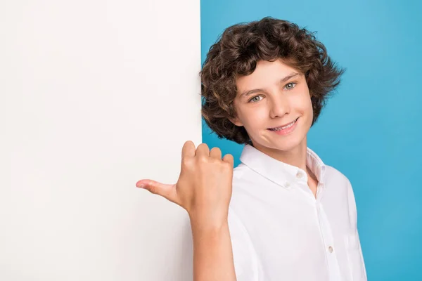 Foto de engraçado menino bonito escola desgaste branco camisa apontando polegar cartaz vazio espaço sorrindo isolado azul cor de fundo — Fotografia de Stock