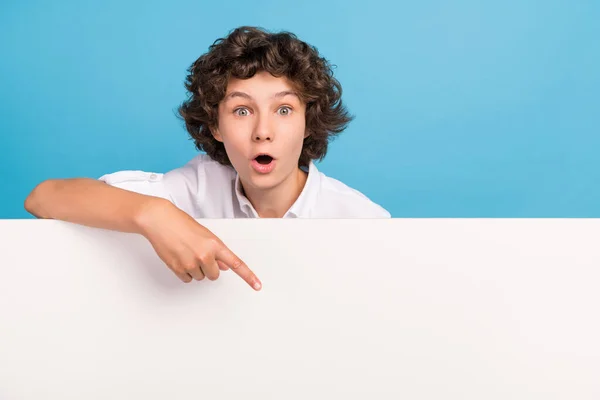 Foto de impressionado engraçado escola menino desgaste branco camisa apontando dedo cartaz vazio espaço isolado azul cor fundo — Fotografia de Stock