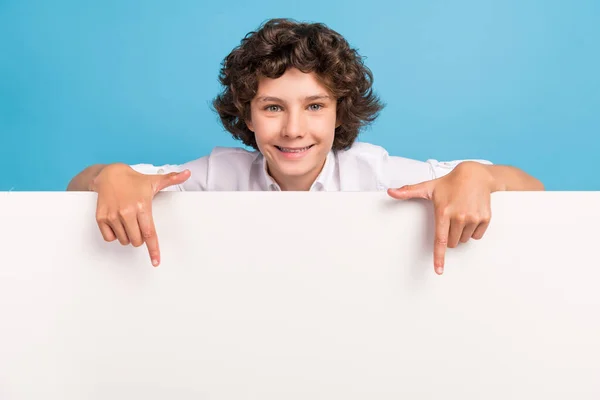 Foto von ziemlich charmanten Schüler tragen weißes Hemd zeigt Finger Plakatwand leeren Raum isoliert blaue Farbe Hintergrund — Stockfoto