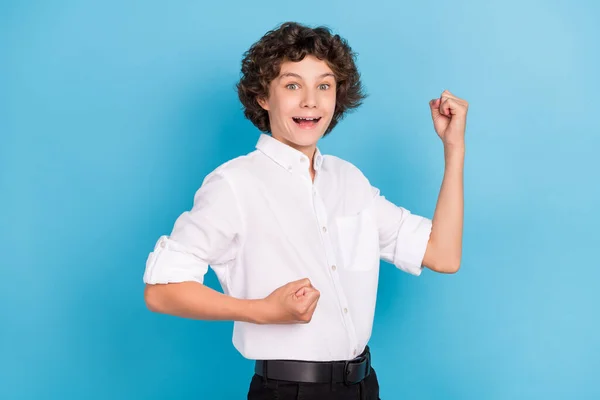 Foto van vrij gelukkig school jongen dragen witte shirt rijzende vuisten glimlachen geïsoleerde blauwe kleur achtergrond — Stockfoto