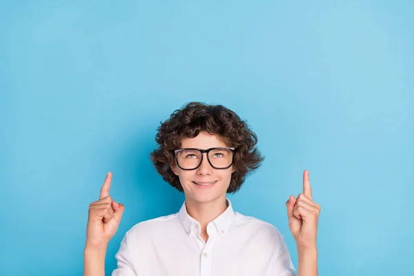 Foto de doce sonhador estudante desgaste branco camisa óculos sorrindo apontando olhando para cima vazio espaço isolado azul cor fundo — Fotografia de Stock