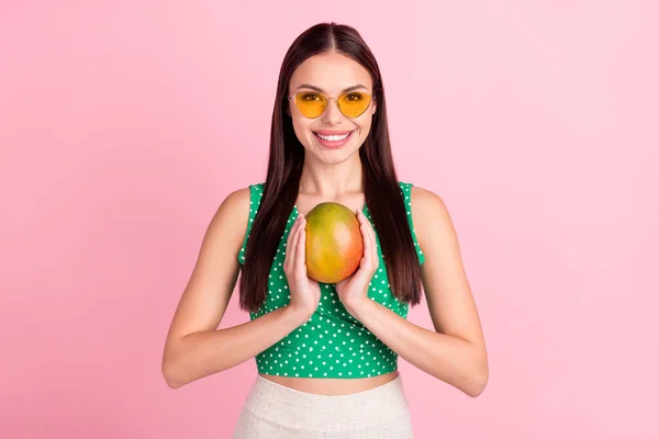 Foto retrato morena sorrindo em vidro solar mantendo suculento manga fruta isolado pastel cor-de-rosa fundo — Fotografia de Stock