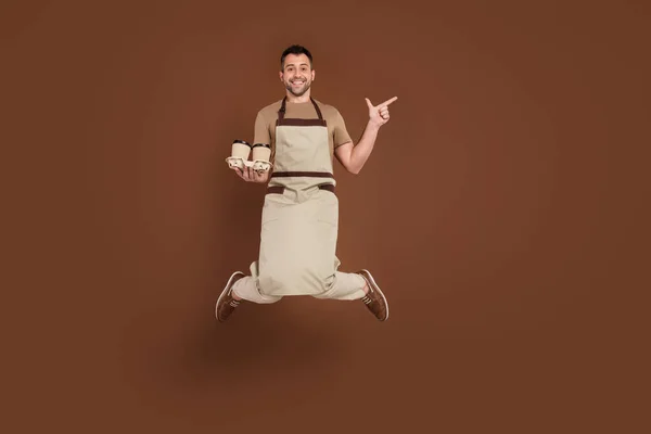 Photo of pretty cute gentleman wear beige apron pointing empty space preparing espresso jumping isolated brown color background — Stock Photo, Image
