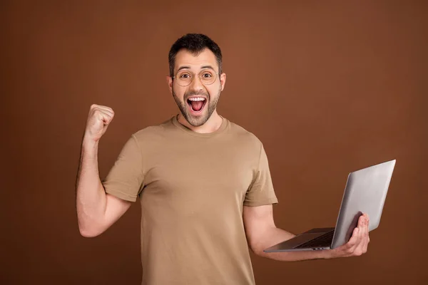 Foto van gelukkige mooie heer dragen beige t-shirt bril met moderne gadget stijgende vuist glimlachende geïsoleerde bruine kleur achtergrond — Stockfoto