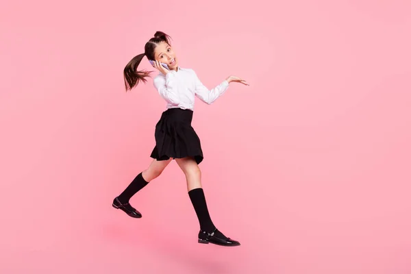 Full längd foto av liten brunett svansar flicka hoppa upp slitage uniform formalwear långa strumpor prata hoppa isolerad på rosa färg bakgrund — Stockfoto