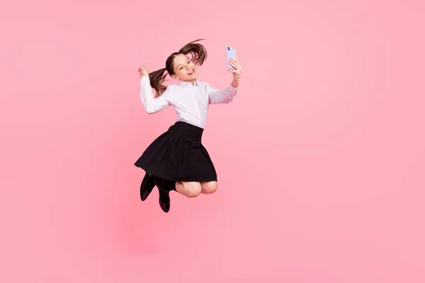 Corpo inteiro foto de marrom rabo de cavalo salto menina fazer selfie telefone desgaste uniforme isolado no fundo cor-de-rosa — Fotografia de Stock