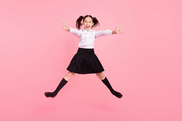 Plná délka fotografie ohromený veselá mladá dívka skočit do rukou nosit uniformu dlouhé ponožky izolované na růžové barevné pozadí — Stock fotografie