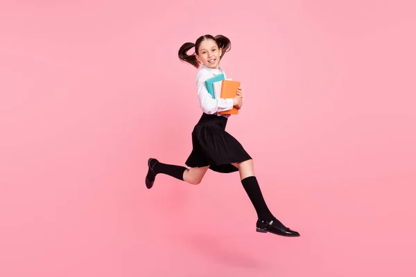 年轻快乐的小女孩跳起来的全长照片拿着抄本笑着穿上粉红色背景的长袜 — 图库照片