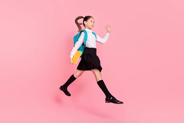 Full length photo of young happy small girl jump up hold copybook wave hello long socks isolated on pink color background — Stock Photo, Image