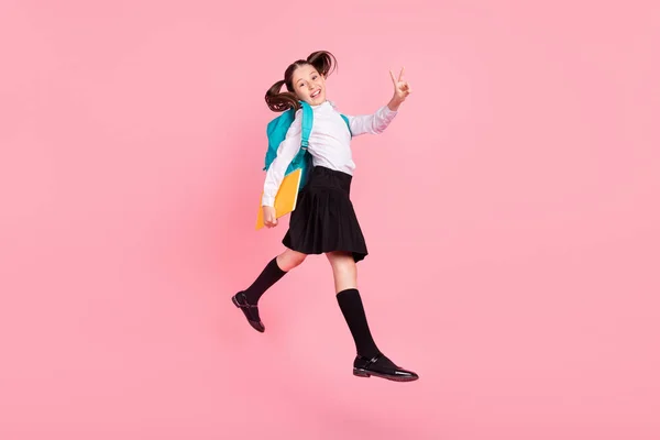 Celé tělo fotografie brunetky ocas holčička skok v-znamení držet copybook skok nahoru izolované na růžové barevné pozadí — Stock fotografie