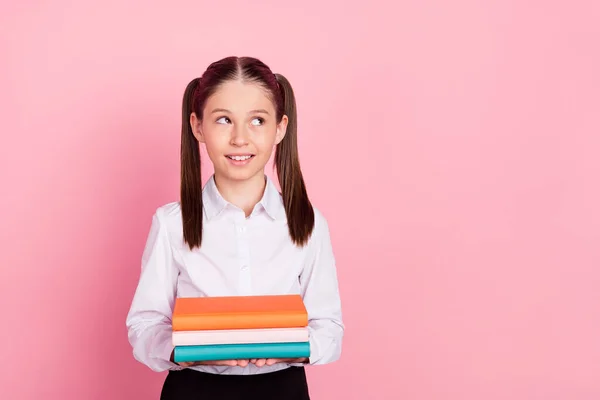 Foto de la joven niña feliz alumna mirada espacio vacío tomarse de la mano libros de texto aislados en el fondo de color rosa —  Fotos de Stock