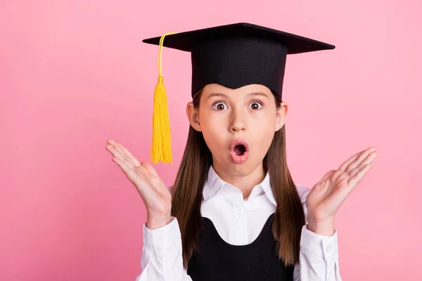 Foto de sorprendido sorprendido feliz positivo niña pequeña usar sombrero de graduado manos excitadas aisladas en el fondo de color rosa —  Fotos de Stock
