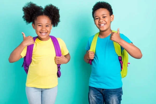 Portret van twee leuke vrolijke kinderen gaan terug naar de lagere school tonen thumbup geïsoleerd over heldere teal turquoise kleur achtergrond — Stockfoto