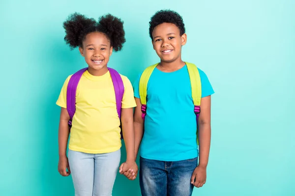 Portré két vonzó vidám gyerekek osztálytársak fogják egymás kezét elszigetelt felett fényes kék türkiz színes háttér — Stock Fotó