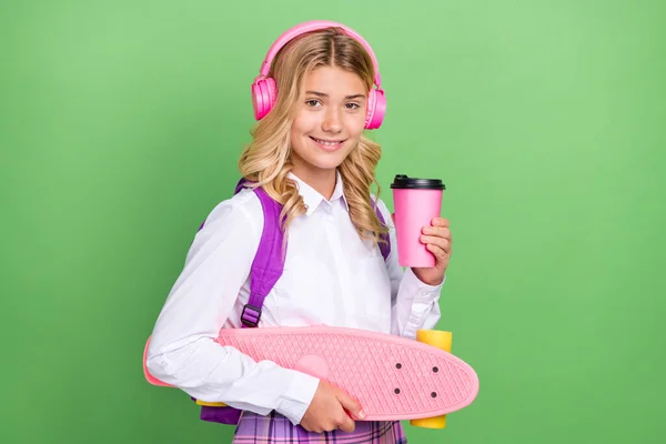 Retrato de menina alegre atraente ouvir melodia beber latte segurando skate isolado sobre fundo de cor verde — Fotografia de Stock