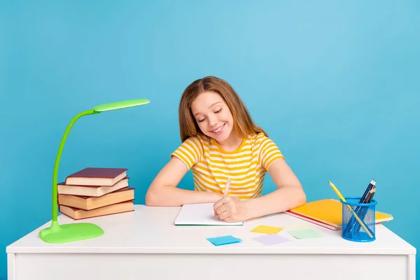 Portret van vrolijke positieve persoon zitten achter tafel houden potlood hebben goed humeur geïsoleerd op blauwe kleur achtergrond — Stockfoto
