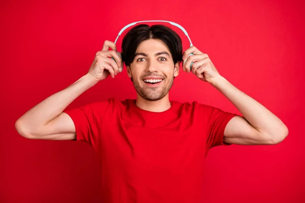 Φωτογραφία του ενθουσιασμένου εμπνευσμένου άντρα απογειωθεί ακουστικά έκπληκτος πρόσωπο φορούν κόκκινο t-shirt απομονωμένο κόκκινο χρώμα φόντο — Φωτογραφία Αρχείου