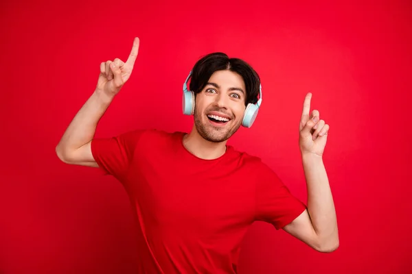 Foto de chico danza disfrutar escuchar música dedo directo espacio vacío usar auriculares camiseta roja aislado fondo de color rojo —  Fotos de Stock