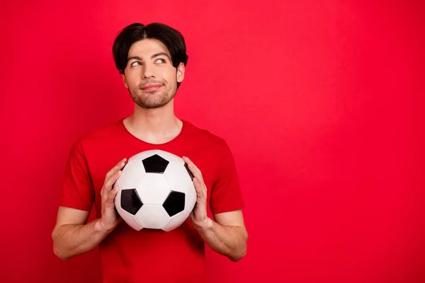 Фото молодого человека счастливой позитивной улыбкой держать футбольный мяч мечты выглядят пустое пространство изолированы на красный цвет фона — стоковое фото