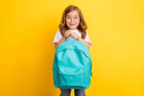 Fotografie veselý dojem školní dívka nosit bílé tričko brýle držení batoh s úsměvem izolované žluté barvy pozadí — Stock fotografie