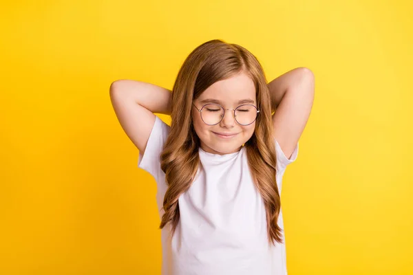 Photo of charming dreamy schoolgirl dressed white t-shirt glasses arms behind head smiling isolated yellow color background — Stock Photo, Image