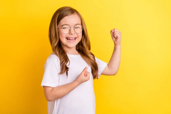 Photo of pretty lucky school girl wear white t-shirt spectacles smiling rising fists isolated yellow color background — Stock Photo, Image