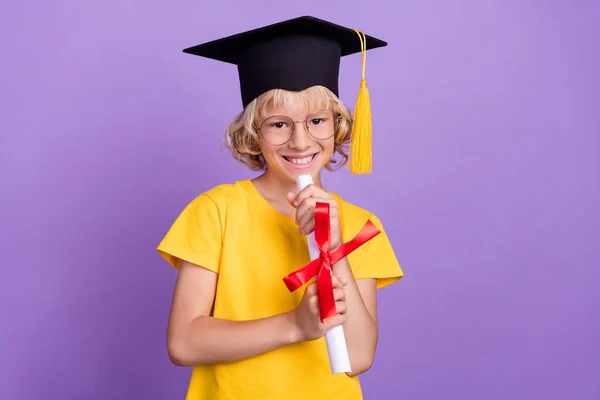 Foto di affascinante grazioso scolaro indossare giallo t-shirt occhiali in possesso di certificato di laurea isolato colore viola sfondo — Foto Stock