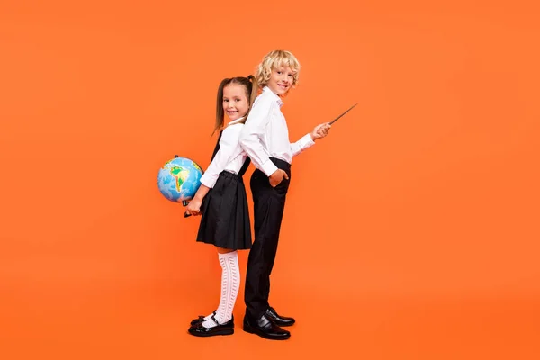 Zdjęcie dwóch uczniów trzymać wskaźnik globu bezpośredni puste miejsce nosić mundur odizolowany pomarańczowy kolor tła — Zdjęcie stockowe