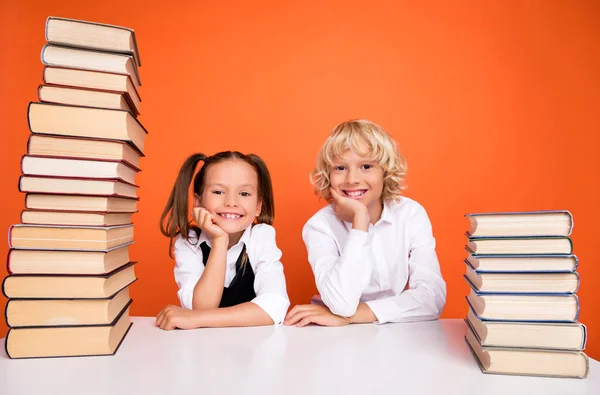 Foto av trevliga glada skolbarn armar haka högen bok bord bära uniform isolerad orange färg bakgrund — Stockfoto