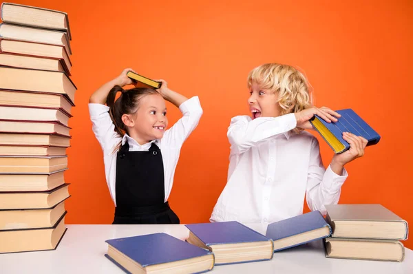 Foto de engraçado tolo louco alunas se divertir jogar pilha livro tabela desgaste uniforme isolado cor de fundo — Fotografia de Stock