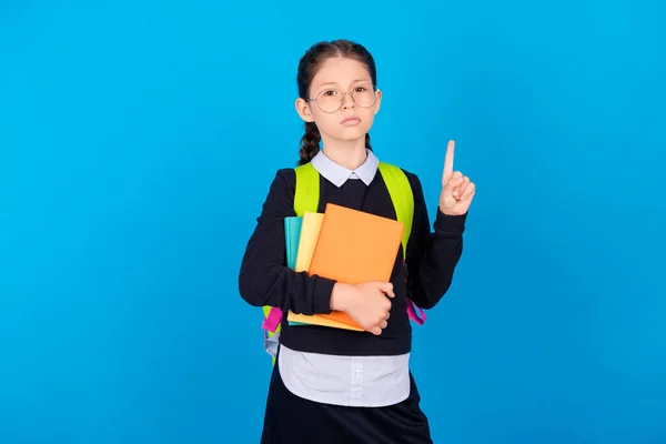 Foto van jonge ernstige schoolmeisje wijs vinger slimme slijtage bril houden leerboek geïsoleerd op blauwe kleur achtergrond — Stockfoto