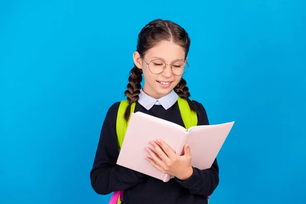 Foto di felice sorridente giovane studentessa in occhiali lettura libro preparare i compiti isolati su sfondo di colore blu — Foto Stock
